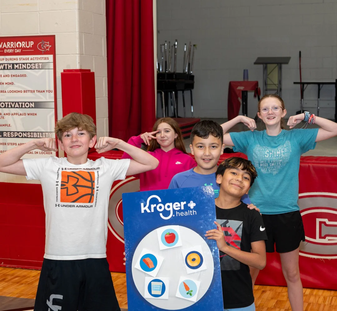 Young students posing triumphantly with Kroger sign